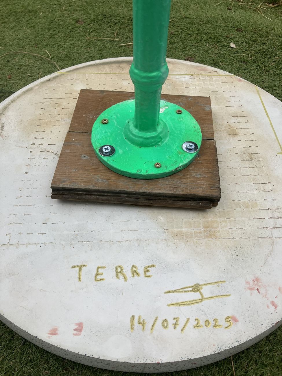 Le dessous du plateau Terre : le nom, la signature et la date 14/07/2025 gravés dans le terrazzo, avec le pied vissé sur une cale en bois de parquet